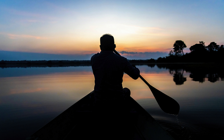 Silhouette eines Mannes, der in der Abenddämmerung auf ruhigem Wasser Kanu fährt
