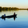 zwei Männer auf einem Boot bei Sonnenuntergang auf dem von Regenwald gesäumten Fluss Guaporé, in der Nähe des abgelegenen Dorfes Mateguá an der Grenze zu Rondônia, Brasilien